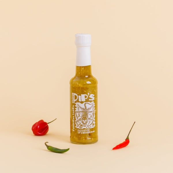 A bottle of "Pip's Fuego del Verde Hot Sauce" with a white cap, standing upright on a light beige background. The bottle is surrounded by three colourful chi;li peppers—red, green, and orange—emphasising the sauce's vibrant, green colour and spicy flavor. The label features a stylised, fierce-looking graphic and the text "It's Green & Mean."