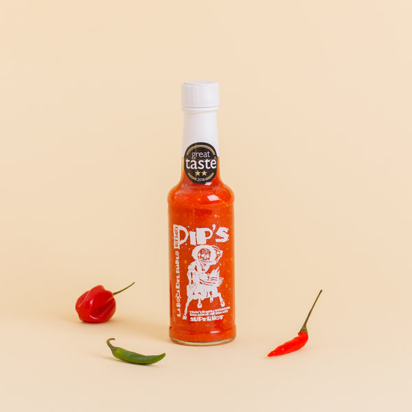 A single bottle of Pip's "La Boca Del Diablo" super hot sauce with a white cap, displayed against a plain background. Surrounding the bottle are three chilli peppers, emphasising its spicy contents. The bottle features a "Great Taste" 2018 award and the iconic skeleton label.
