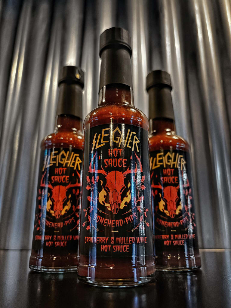 Three bottles of Sleigher limited edition cranberry and mulled wine hot sauce by Bonehead and Pip's, displayed in front of a metallic backdrop.