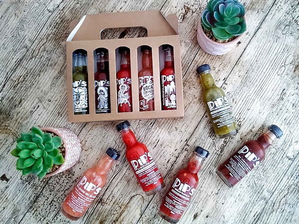 A hot sauce gift set featuring a variety of Pip's sauces, displayed on a rustic wooden table with potted succulents in the background.