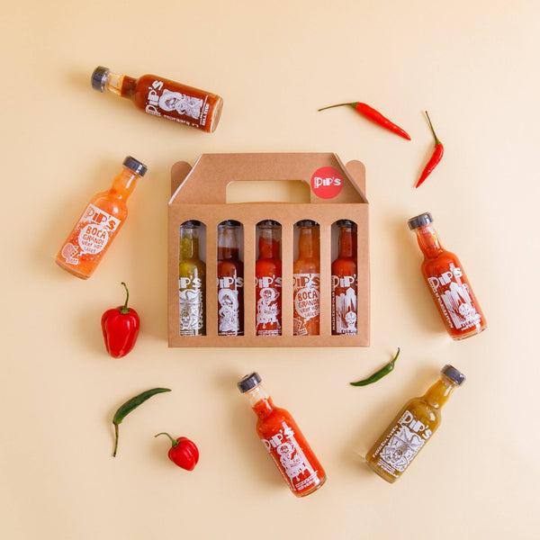 A beautifully arranged hot sauce set with six mini bottles of Pip's sauces, surrounded by fresh chillies and a simple backdrop.