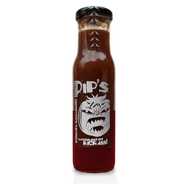 A bottle of Pip's Tomate Assassino spicy tomato ketchup, filled with deep red sauce. The label shows an aggressive face design and the phrase "Ketchup just got kick ass!" in bold white text.